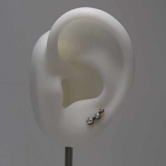 White ear model with a silver earring with three rhinestones in a row on a gray background