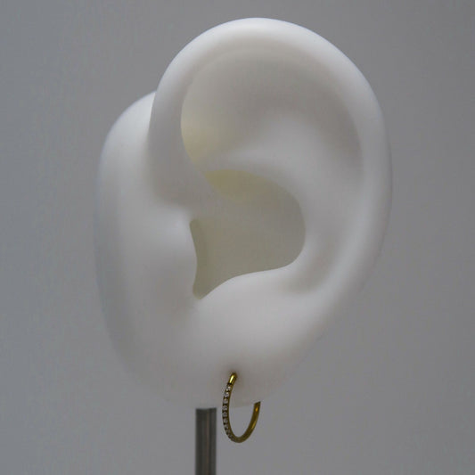 White ear model with a small gold rhinestone hoop on a gray background