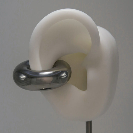 White ear model with a large silver circular earring cuff on a gray background