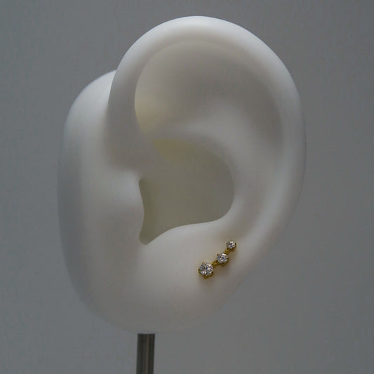 White ear model with a gold earring with three rhinestones in a row on a gray background