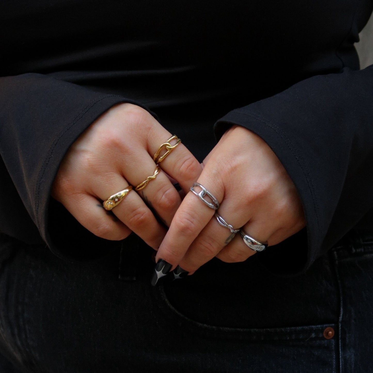 Close-up of hands with multiple rings on fingers, wearing a dark jacket.