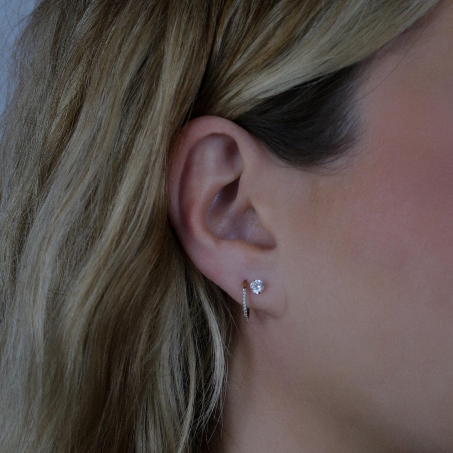 Close-up of an ear wearing a rhinestone earring and a rhinestone hoop earring