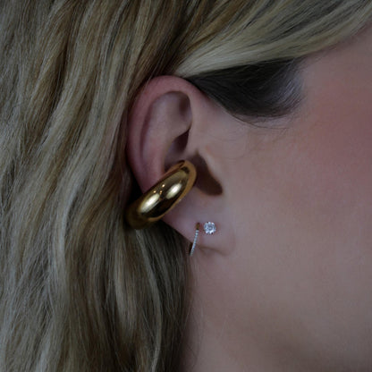 Close-up of an ear with the gold earring cuff and two small earrings.