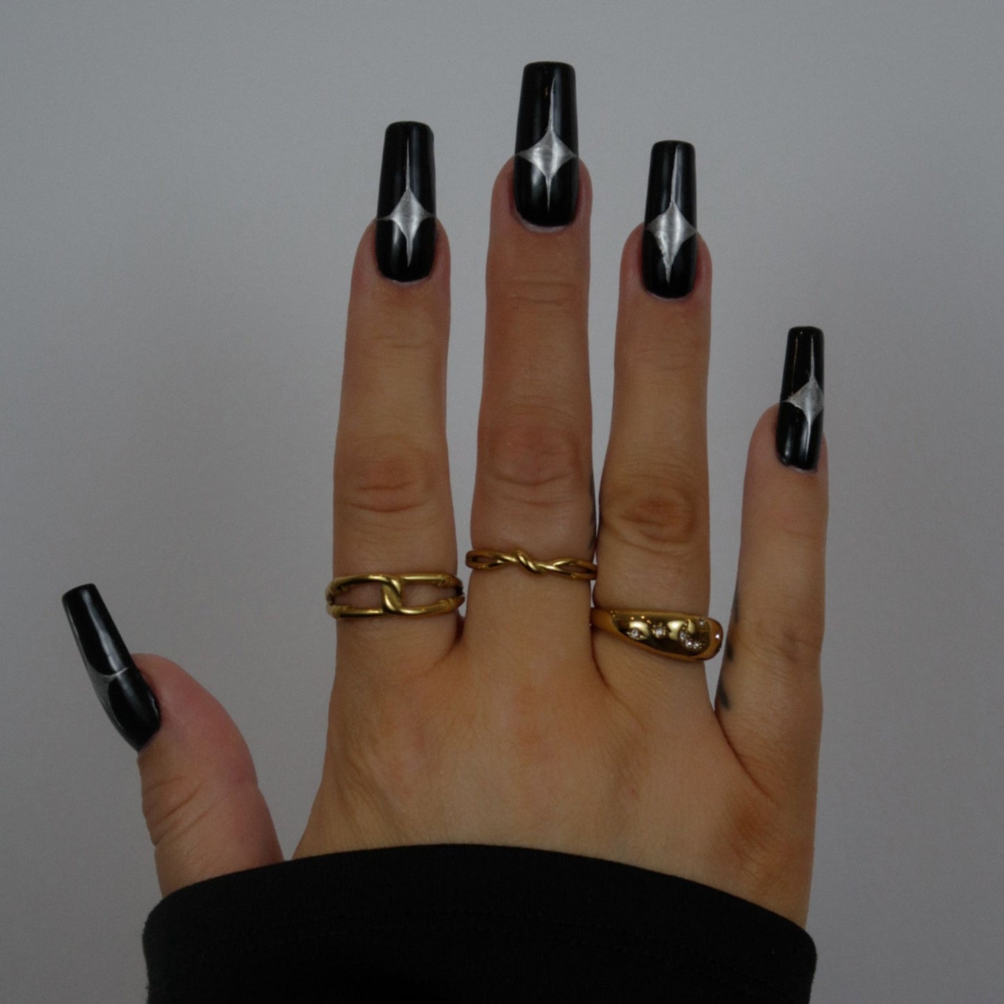 Hand with black nail polish and gold rings on a plain background