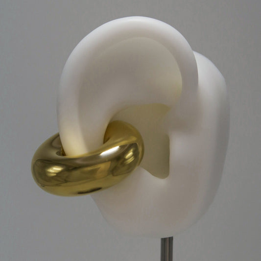 White ear model with a large gold circular earring cuff on a gray background