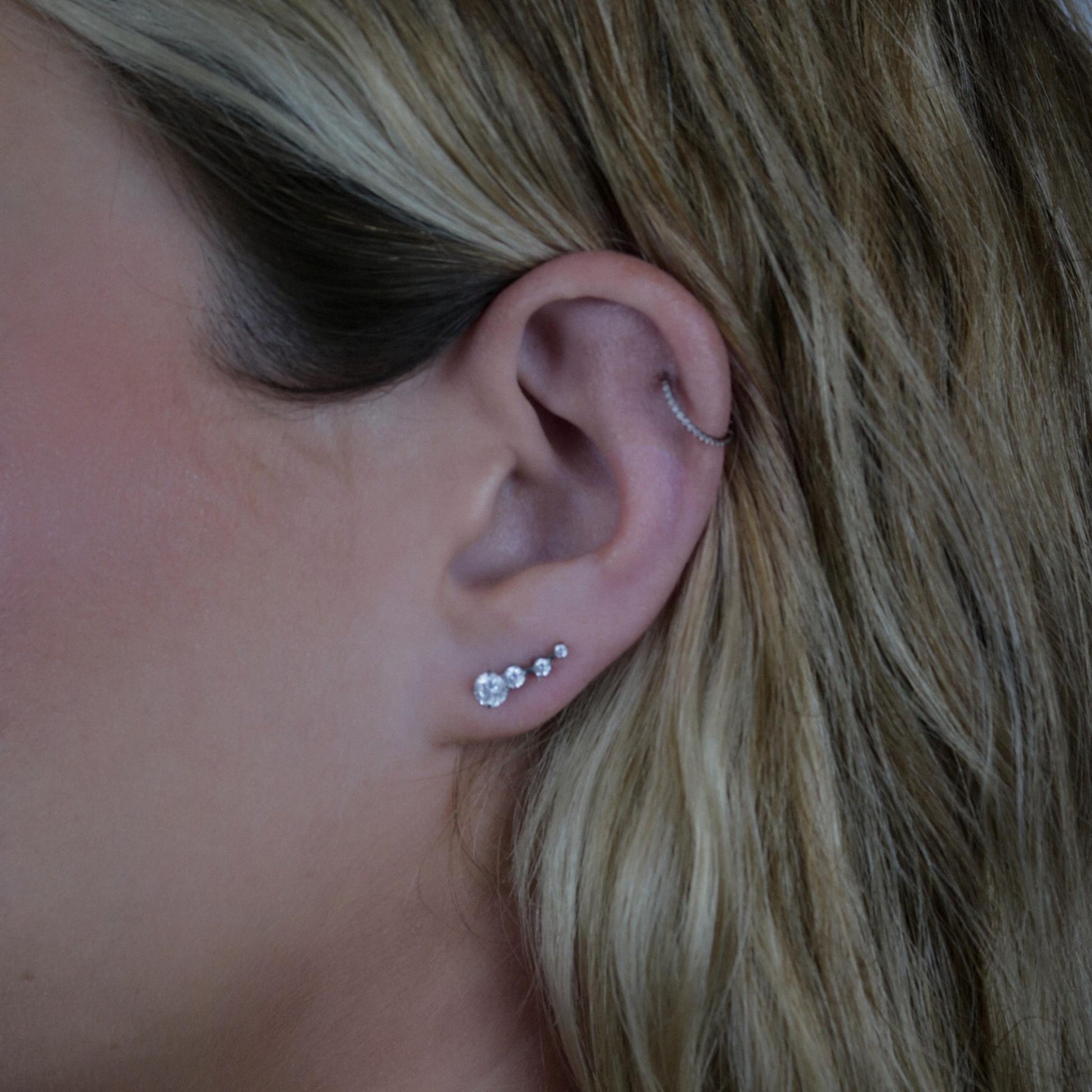 Close-up of an ear with multiple earrings against a neutral background