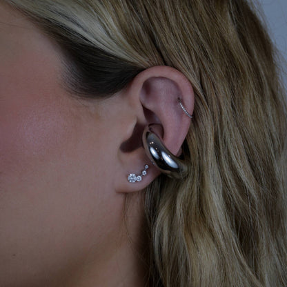 Close-up of an ear with the silver earring cuff and three small earrings.