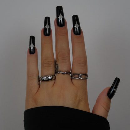 Hand with black nail polish and silver rings on a plain background
